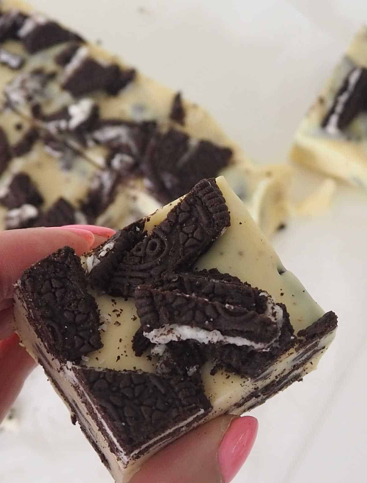 Adult with pink nail polish holding a slice of white chocolate and Oreo fudge.