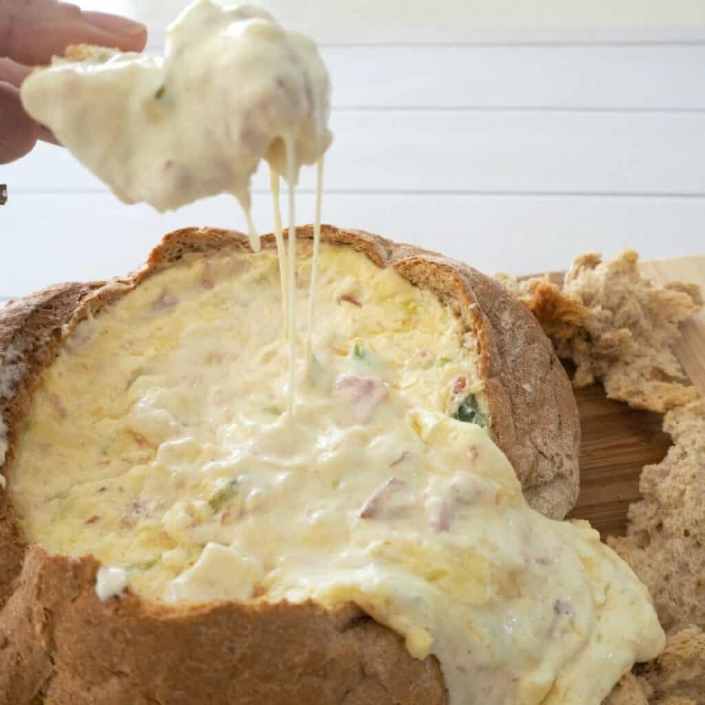 Bread scooping up cheese and bacon cob loaf dip