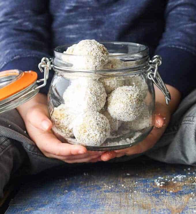 Tropical oat balls in a glass jar held by a child.