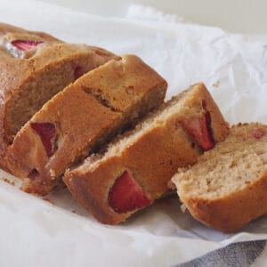Slices of Banana and Strawberry Loaf sitting on a sheet of baking paper which is on top of a blue check tea towel.