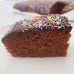 Side view of a slice of chocolate cake with chocolate icing and sprinkles