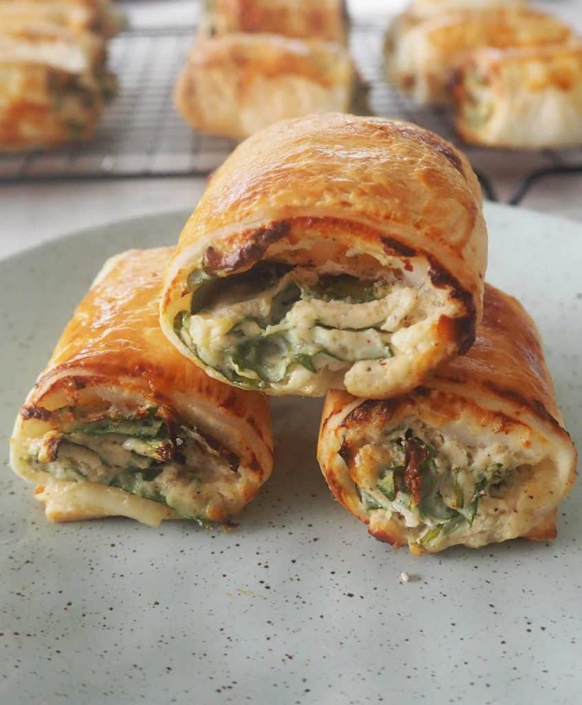 Close up of three spinach and ricotta rolls stacked on a green plate.