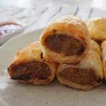 Three Thermomix Sausage Rolls on a speckled plate. In the background is a small bowl of sauce.