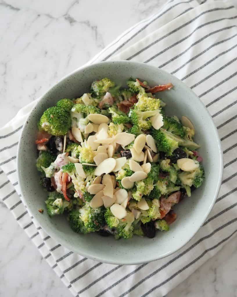 Overhead view of broccoli salad with cranberry and bacon in a green bowl on a marble backdrop
