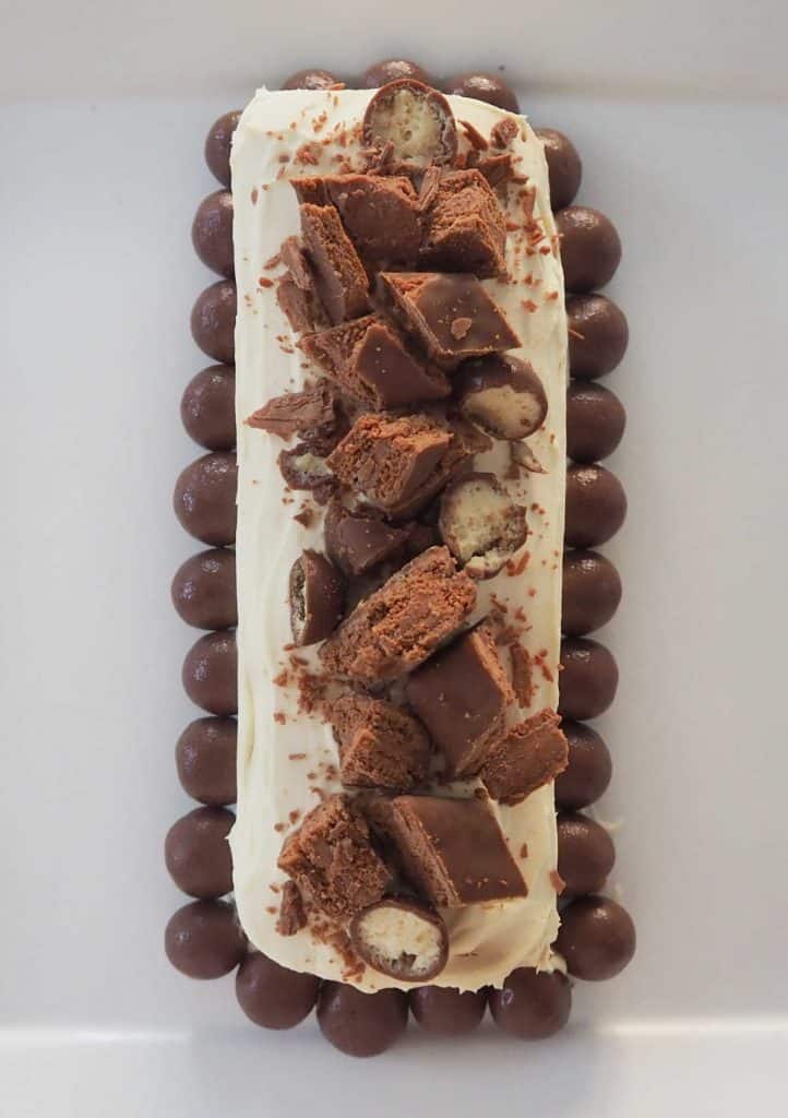overhead view of chocolate ripple cake which has been decorated with tim tams and maltesers on a white platter
