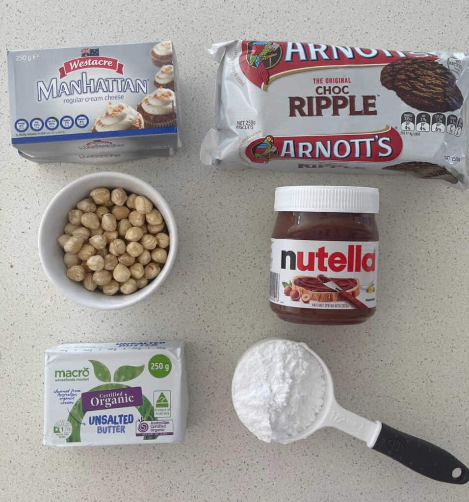 Ingredients to make a Nutella Cheesecake sitting on a speckled stone bench top.