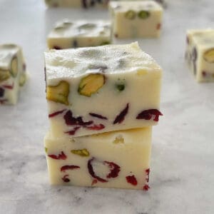 2 pieces of white chocolate christmas fudge stacked on top of each other on a marble background.