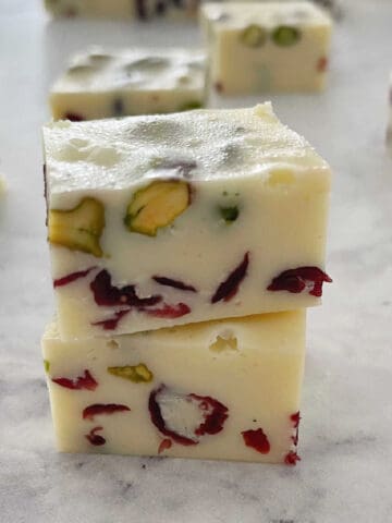 2 pieces of white chocolate christmas fudge stacked on top of each other on a marble background.
