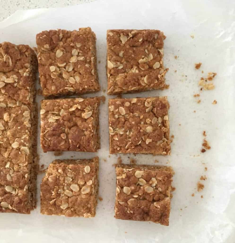 Pieces of anzac slice sitting on a sheet of greaseproof paper