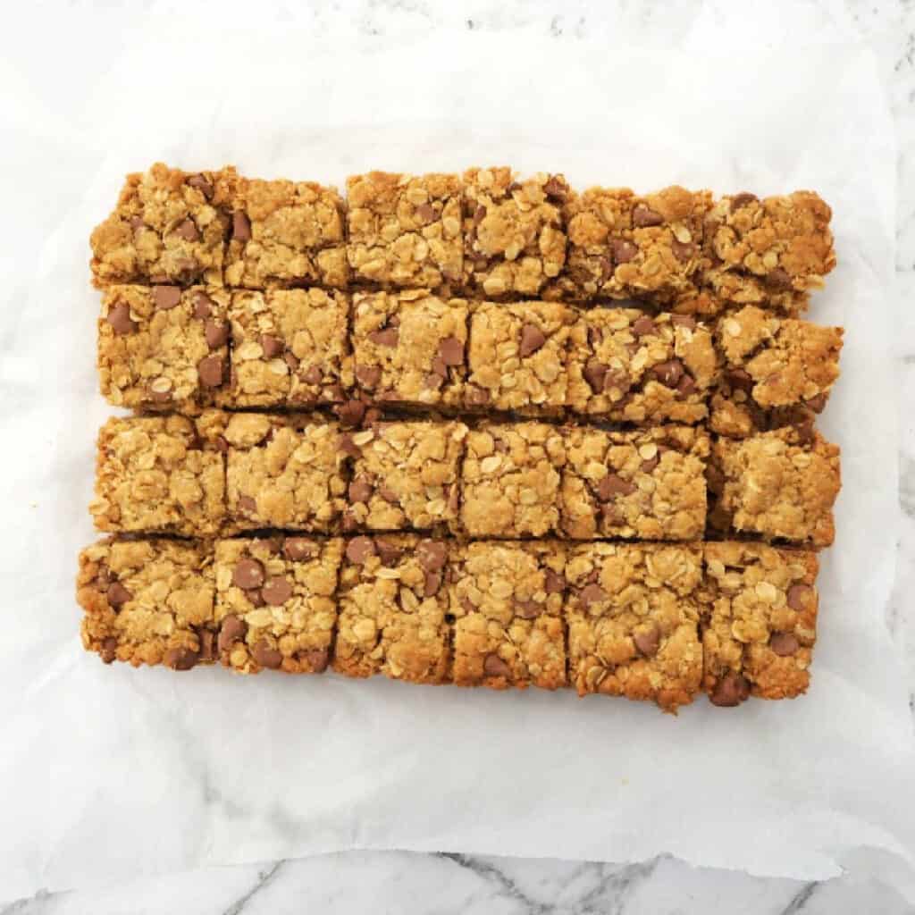 Sliced Chocolate Chip Anzac Slice on baking paper on a marble background