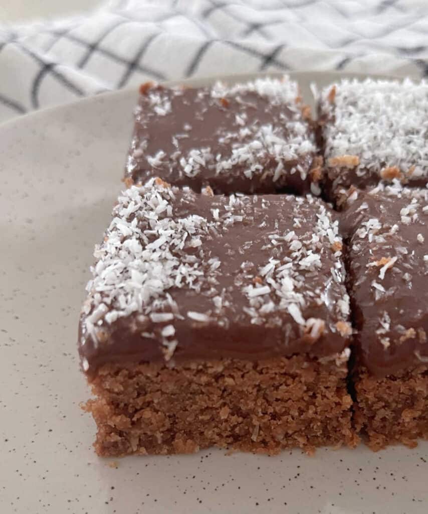 side view of three pieces of chocolate coconut slice on a speckled plate.