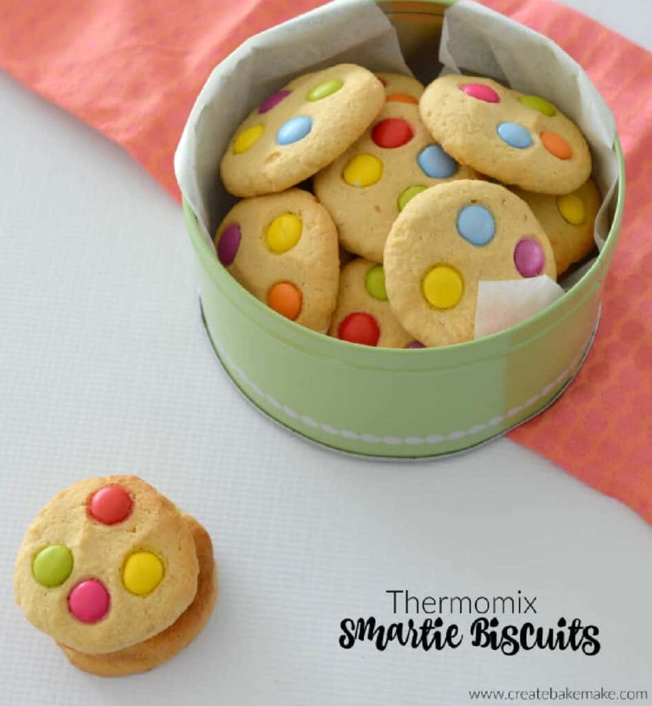 2 smartie cookies stacked on top of each other in from to green tin with more cookies sitting on a pink towel.