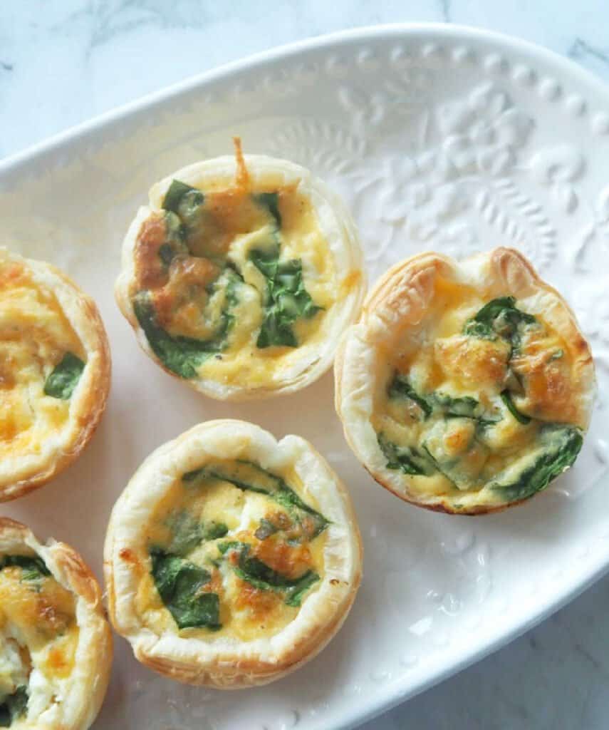 Overhead view of spinach and feta mini quiche on a white platter.