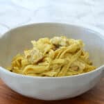 side view of Creamy Chicken Pesto Pasta in a speckled bowl on a wooden tray.