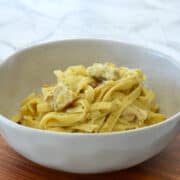 side view of Creamy Chicken Pesto Pasta in a speckled bowl on a wooden tray.