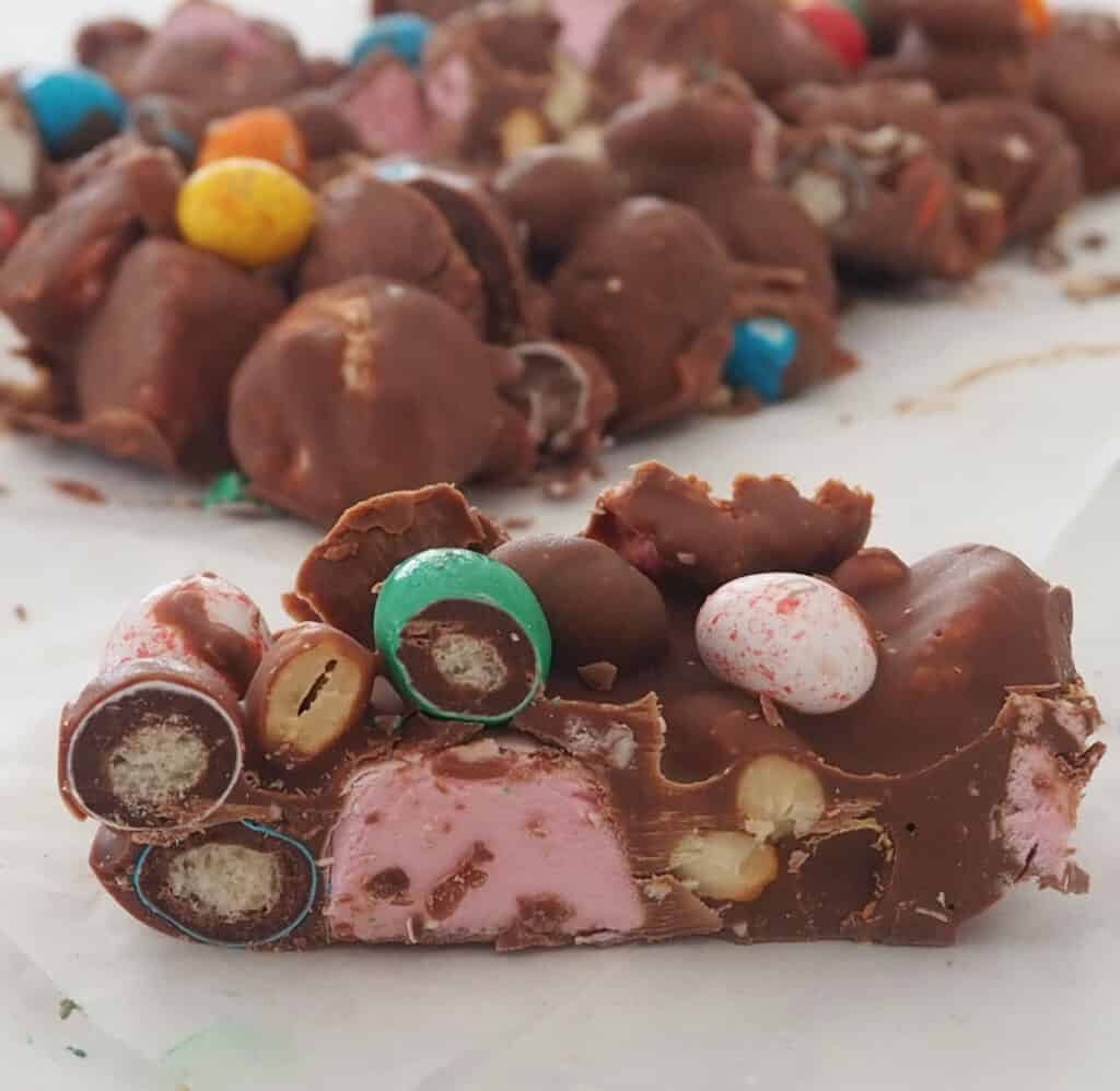 Slice of rocky road sitting on baking paper with more rocky road behind it.
