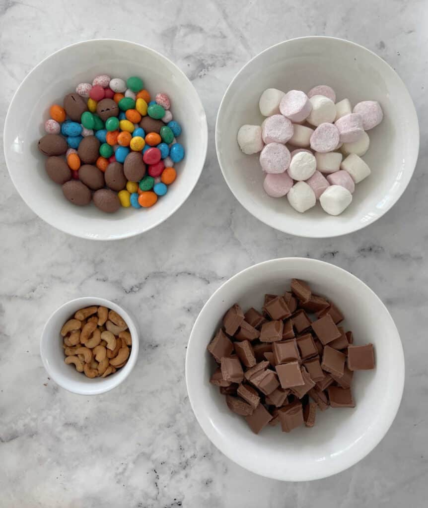 Easter Egg Rocky Road Ingredients sitting in white bowls on a marble backdrop.