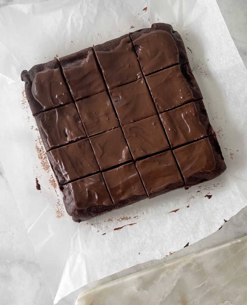 Chocolate brownies cut into squares sitting on apiece of baking paper.