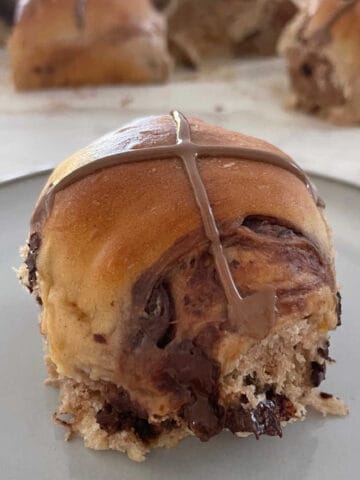 Choc Chip Hot cross Bun on a grey plate with hot cross buns in the background.