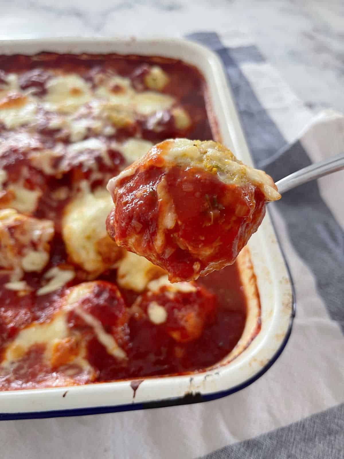 spoon holding a baked chicken parma ball with a tray in the background.