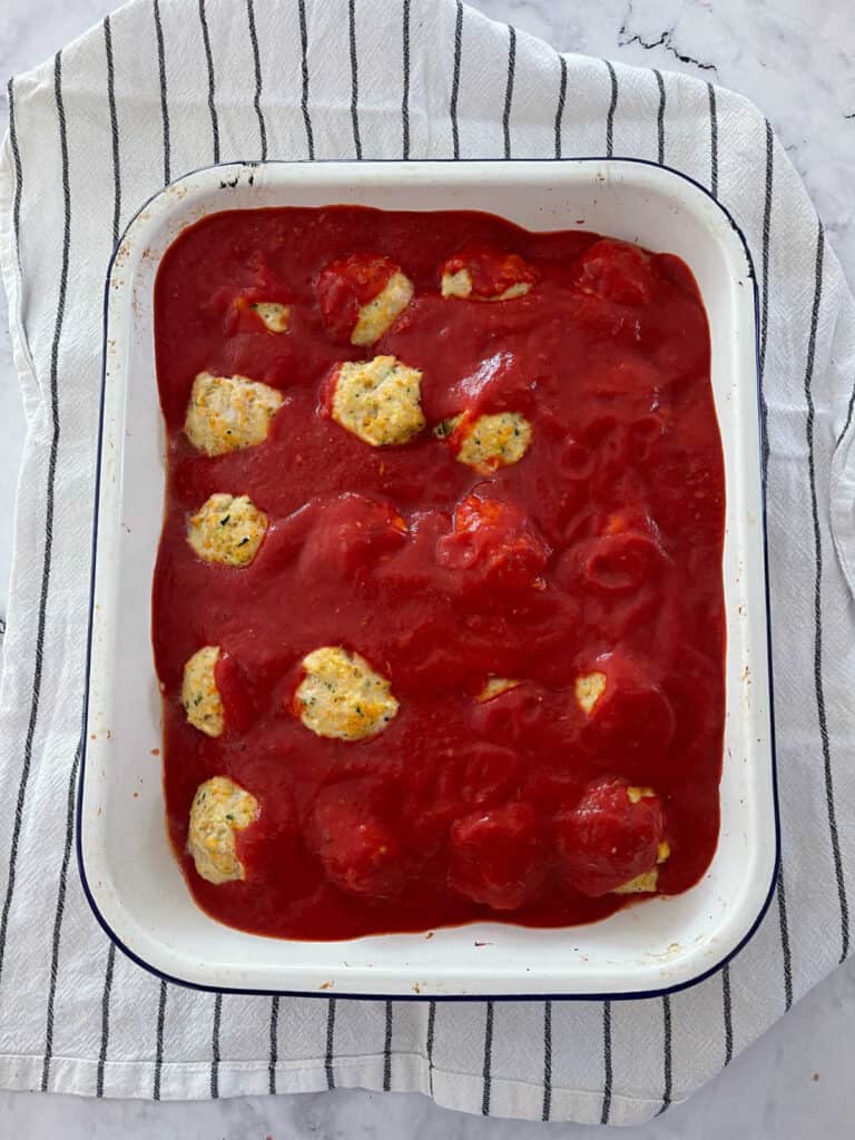 Chicken parma balls in baking tray with sauce added.