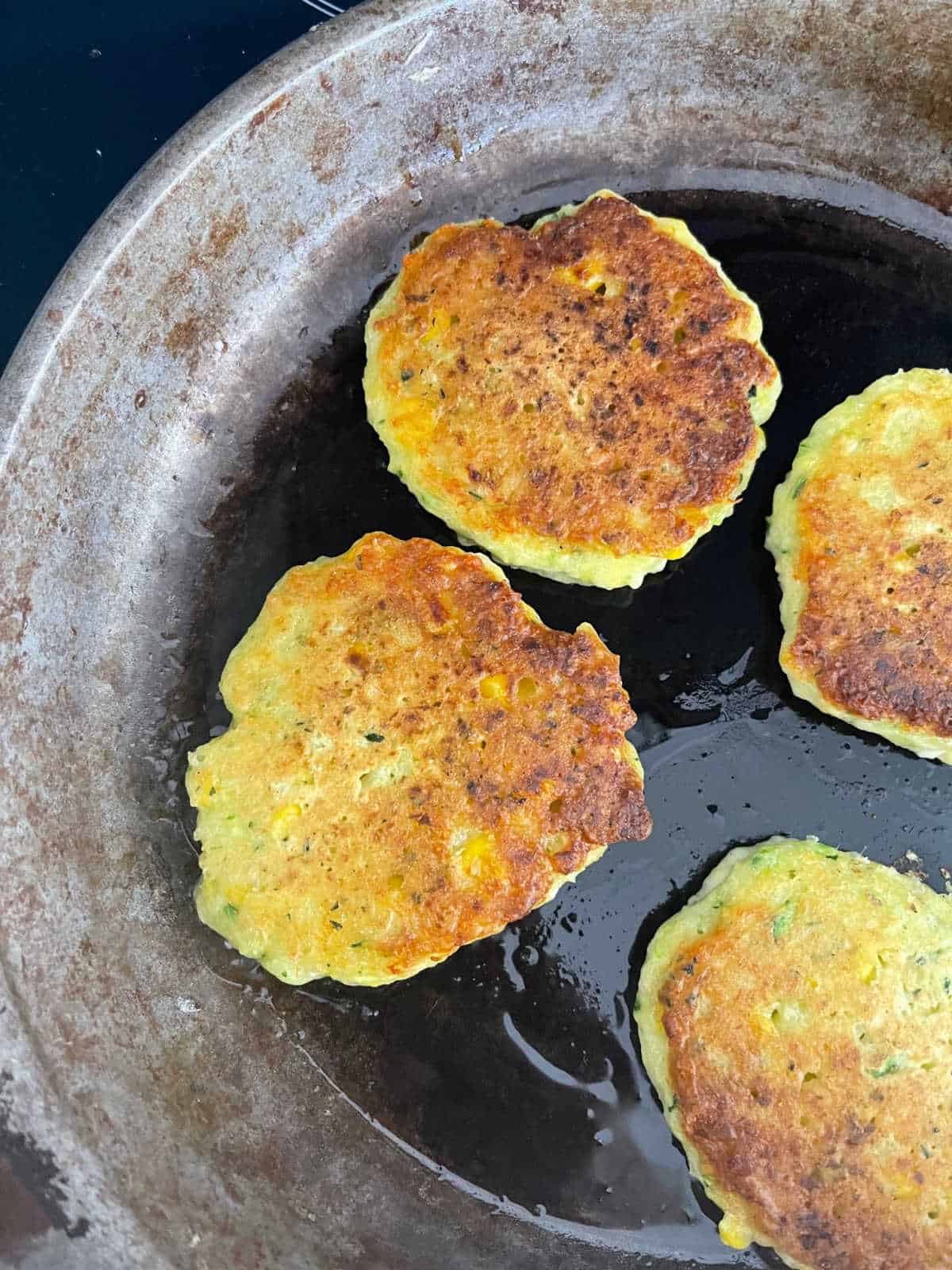 corn and zucchini fritters cooking in a cast iron pan.
