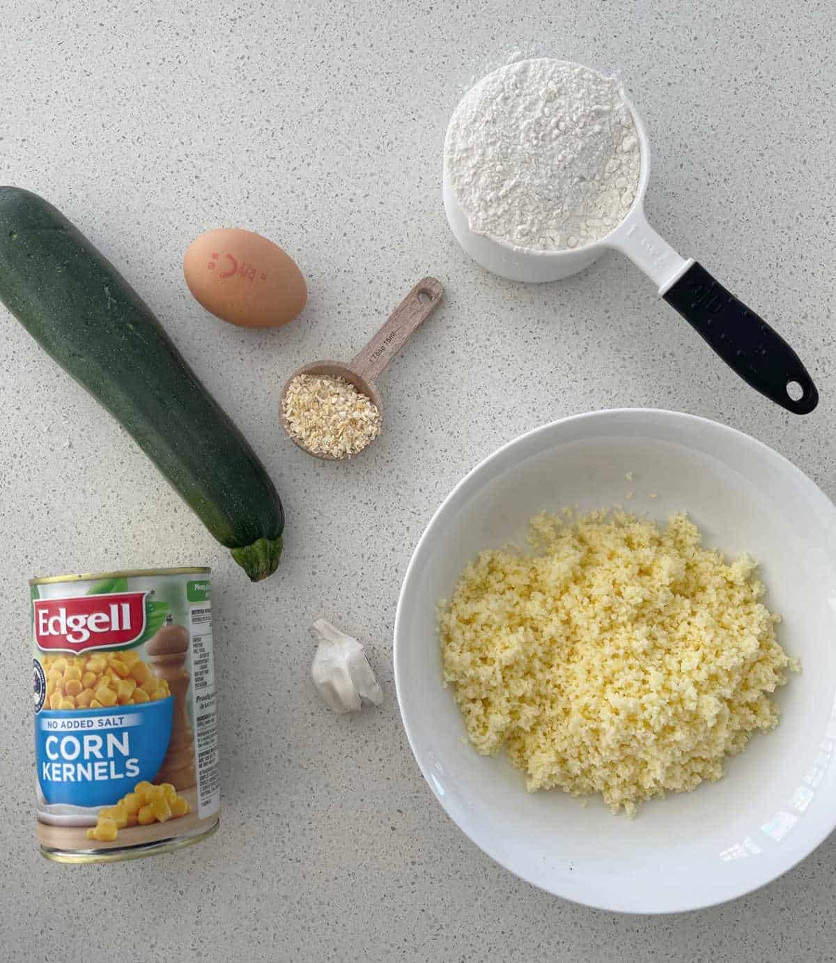 ingredients to make corn and zucchini fritters on a speckled bench.