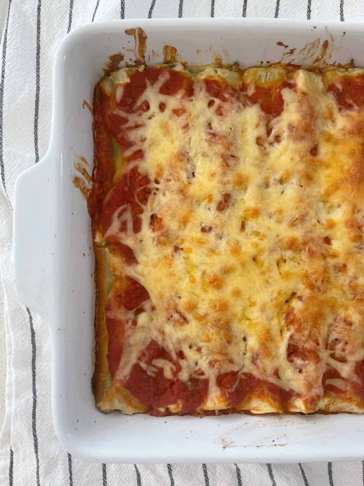 Baked Spinach and Ricotta Cannelloni in baking dish sitting on a blue and white striped towel.