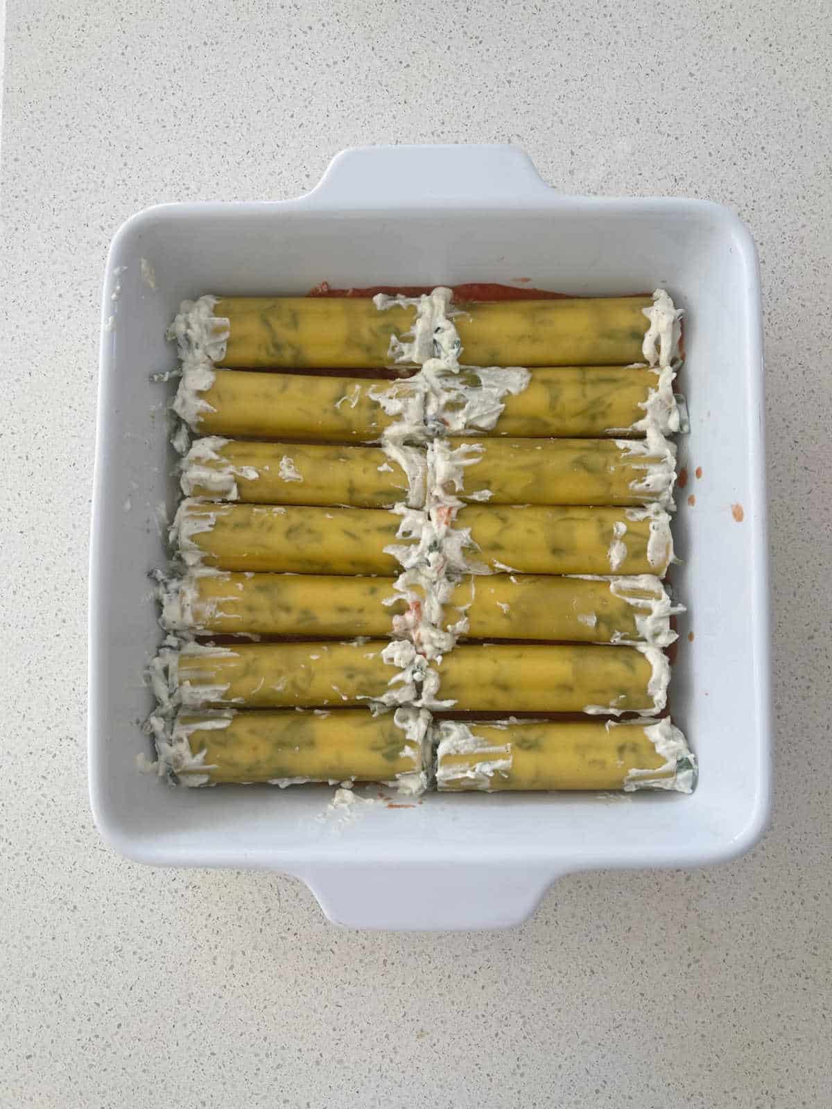 Uncooked spinach and ricotta cannelloni in a white baking dish.