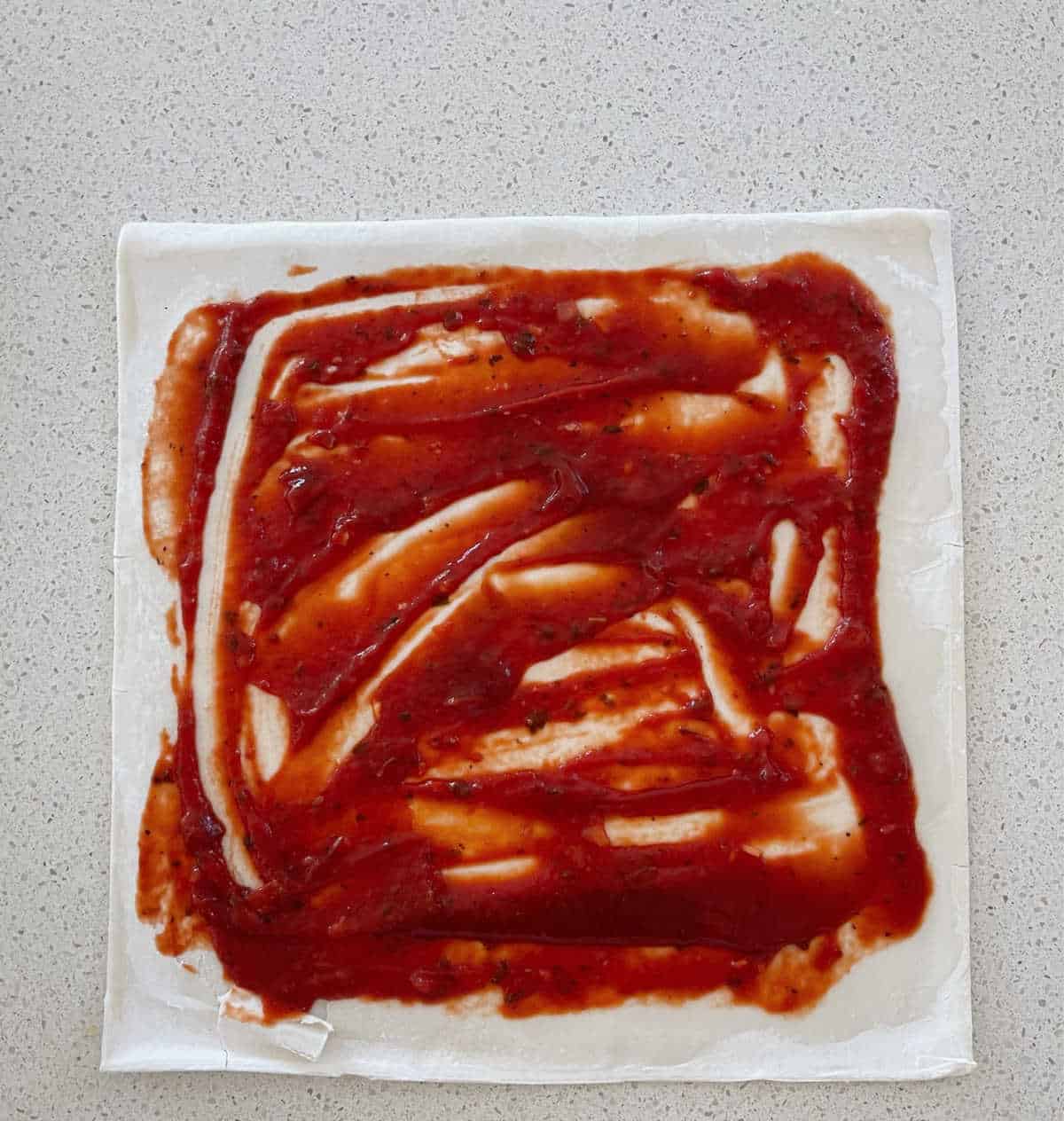 sheet of puff pastry covered with pizza sauce.