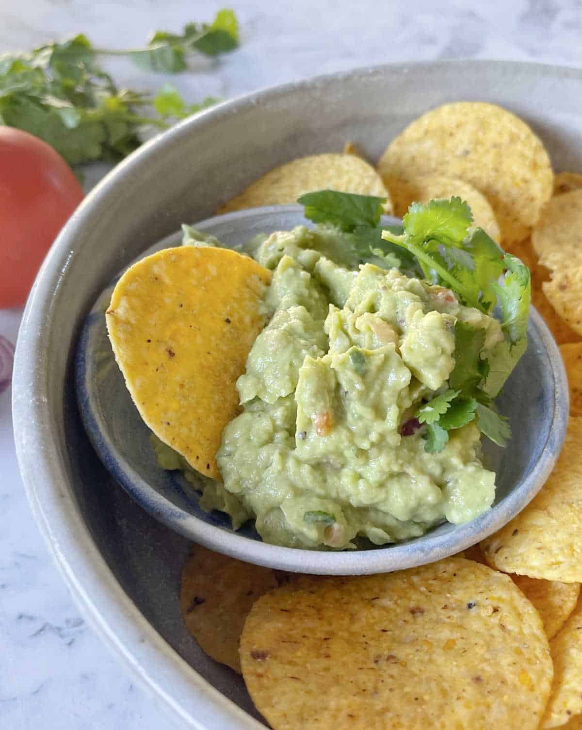 Guacamole in a small bowl sitting inside a large bowl of corn chips.