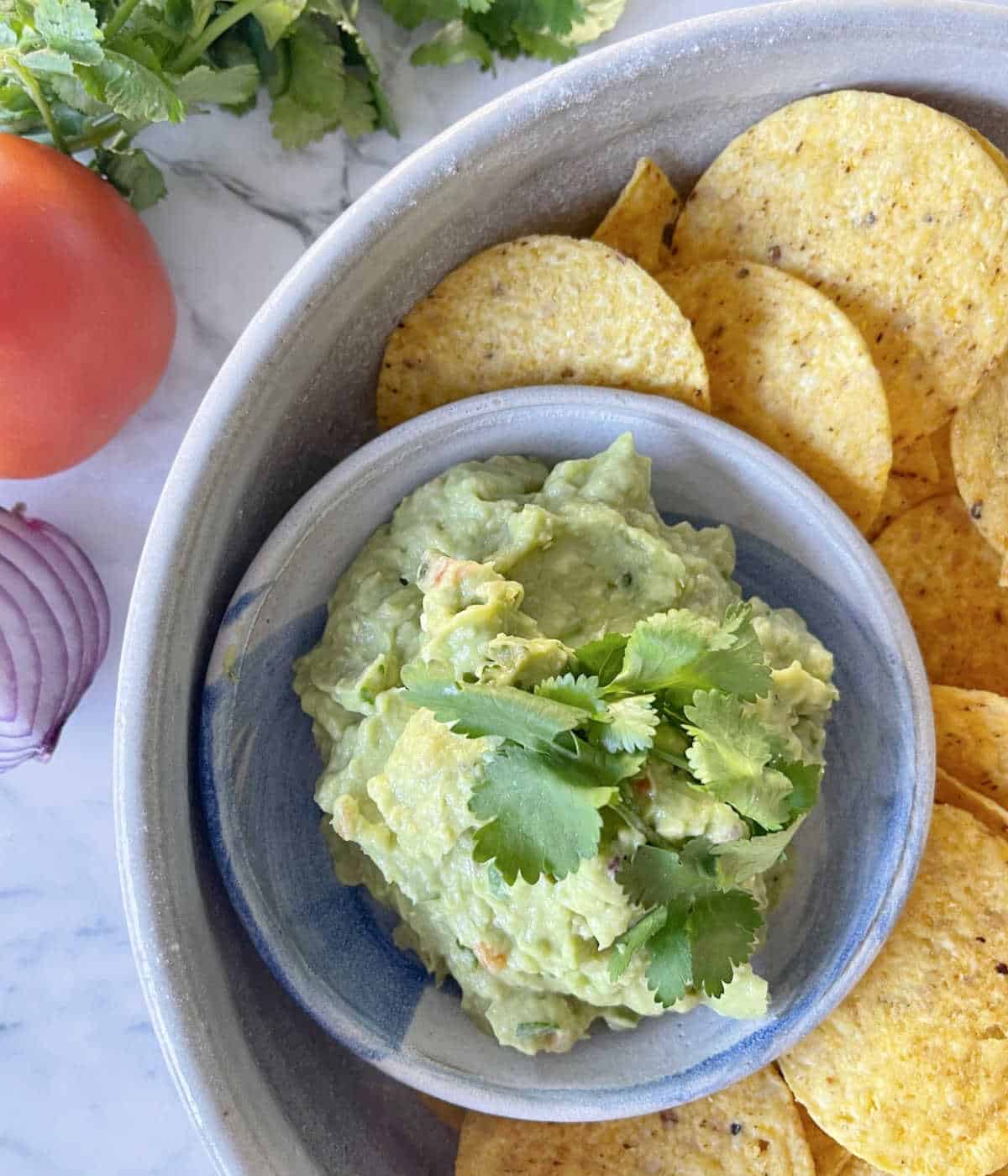 Guacamole in a small bowl sitting inside a large bowl of corn chips.