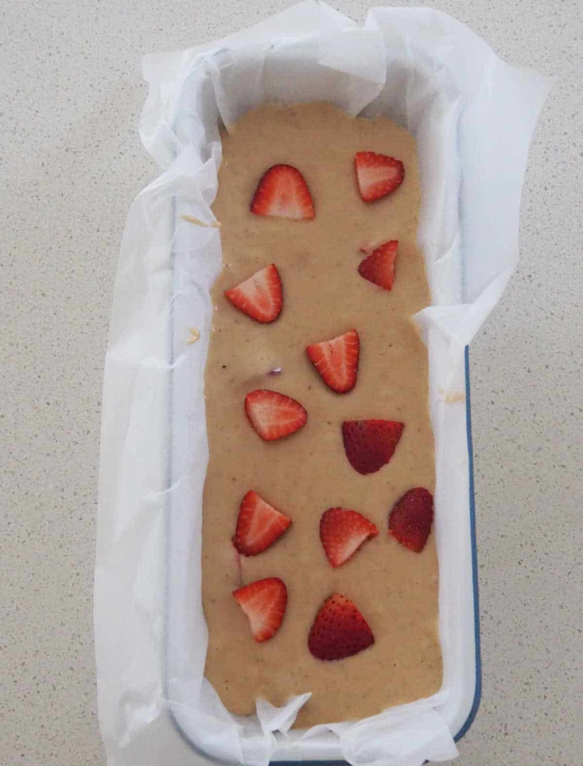 Banana and Strawberry Bread mixture topped with strawberries in a loaf pan lined with baking paper.
