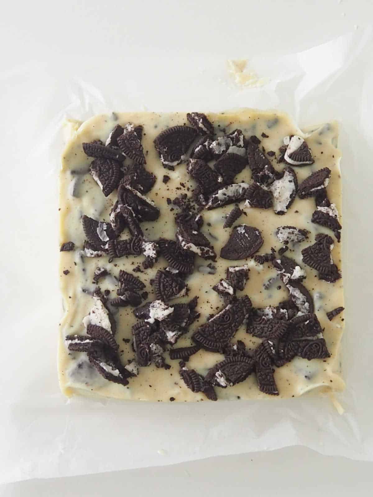 An uncut slab of white chocolate and Oreo fudge that is sitting on baking paper on top of a white bench top.