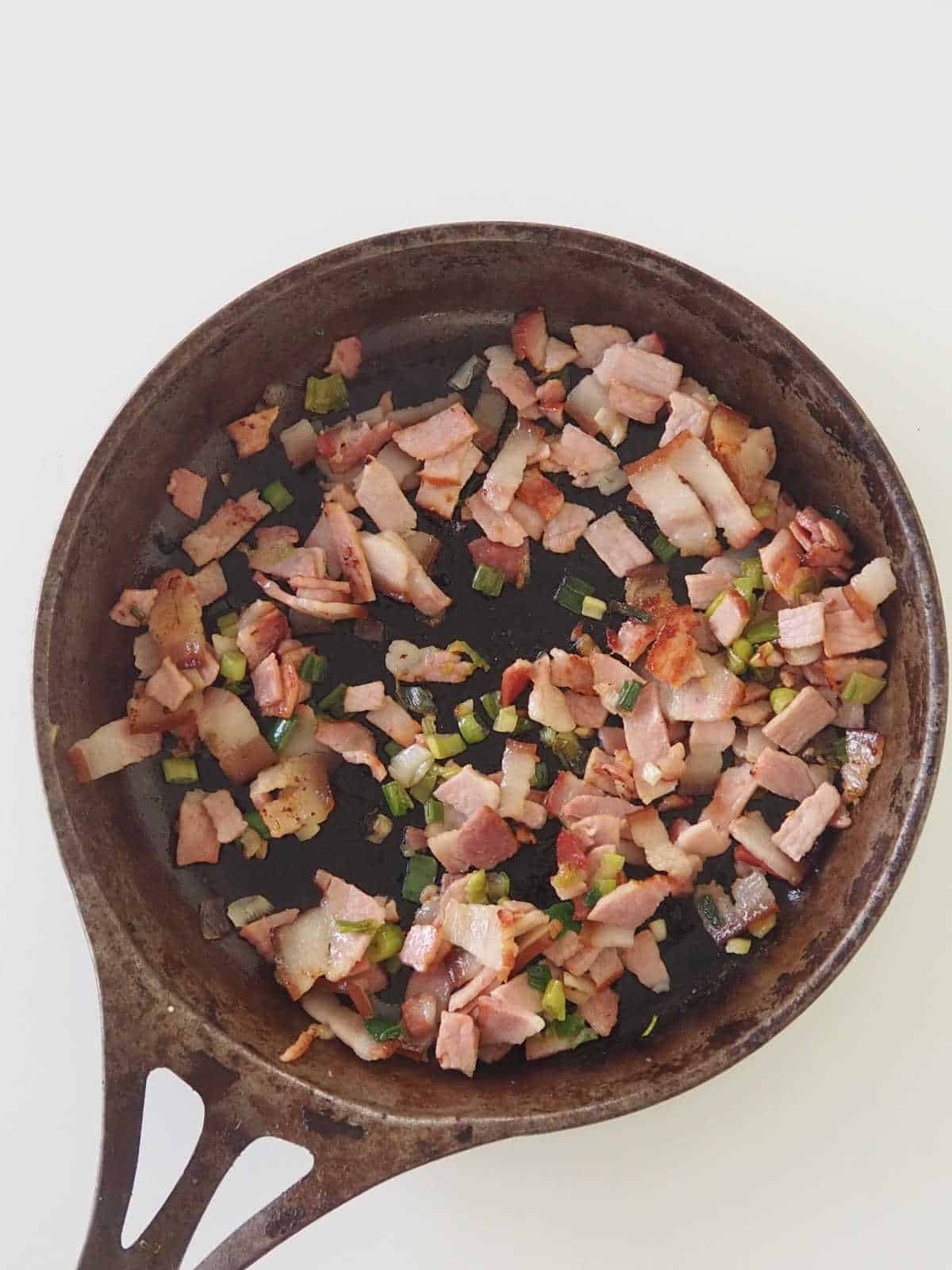 cooked bacon and spring onion in a frying pan.