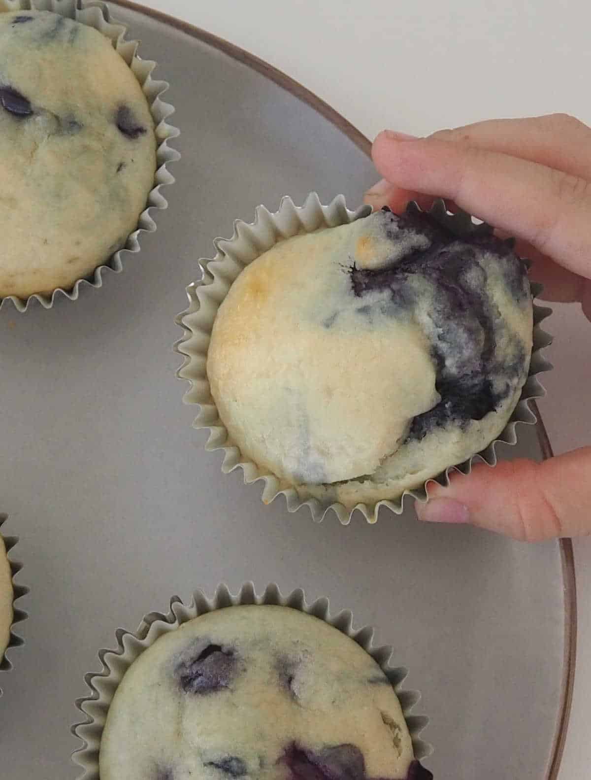 child's hand reaching for a blueberry muffin.