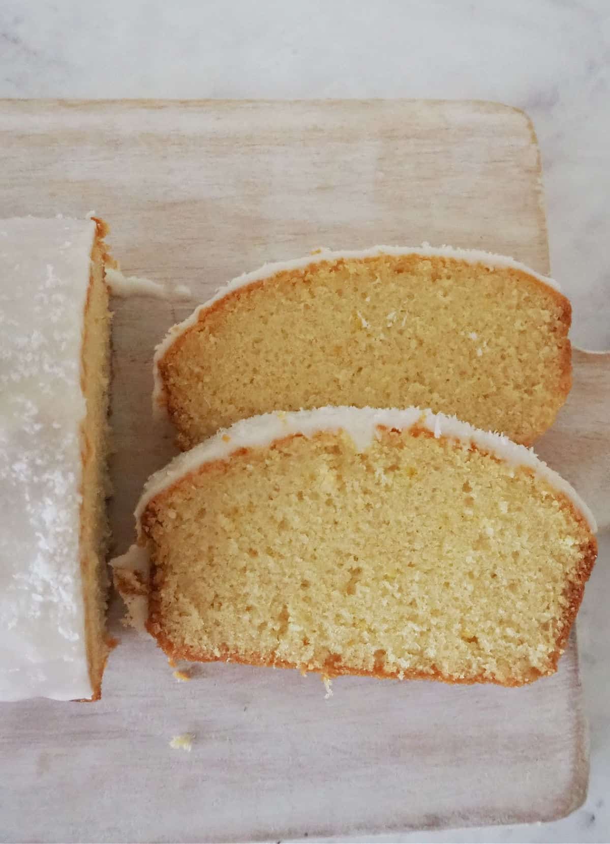 Overhead view of Lemon Butter Cake Sliced and sitting on a pale wooden board.