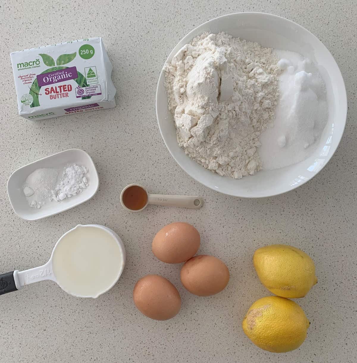 Ingredients to make a Lemon Butter Cake sitting on a stone bench top.
