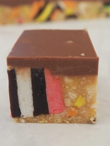 A piece of Licorice Slice sitting on a white bench top with other pieces of slice behind it