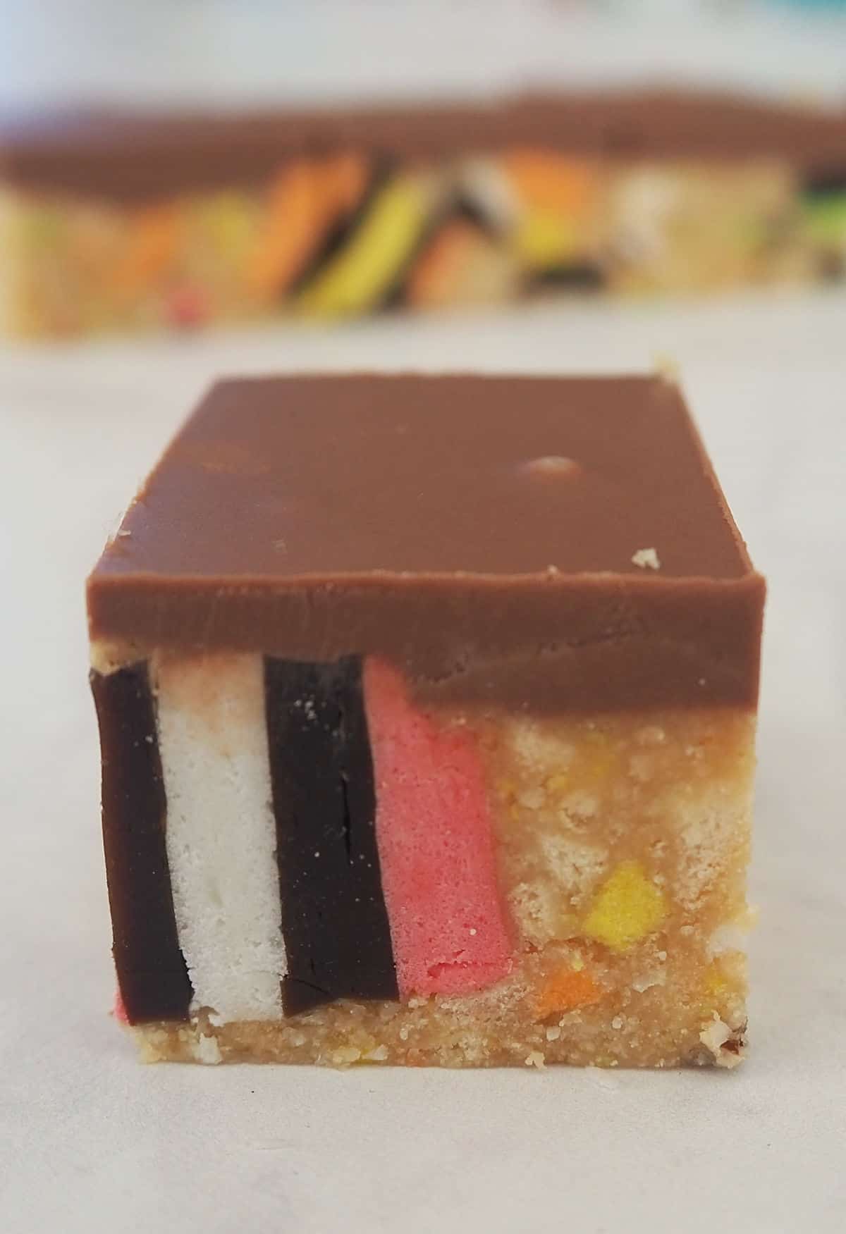 A piece of Licorice Slice sitting on a white bench top with other pieces of slice behind it