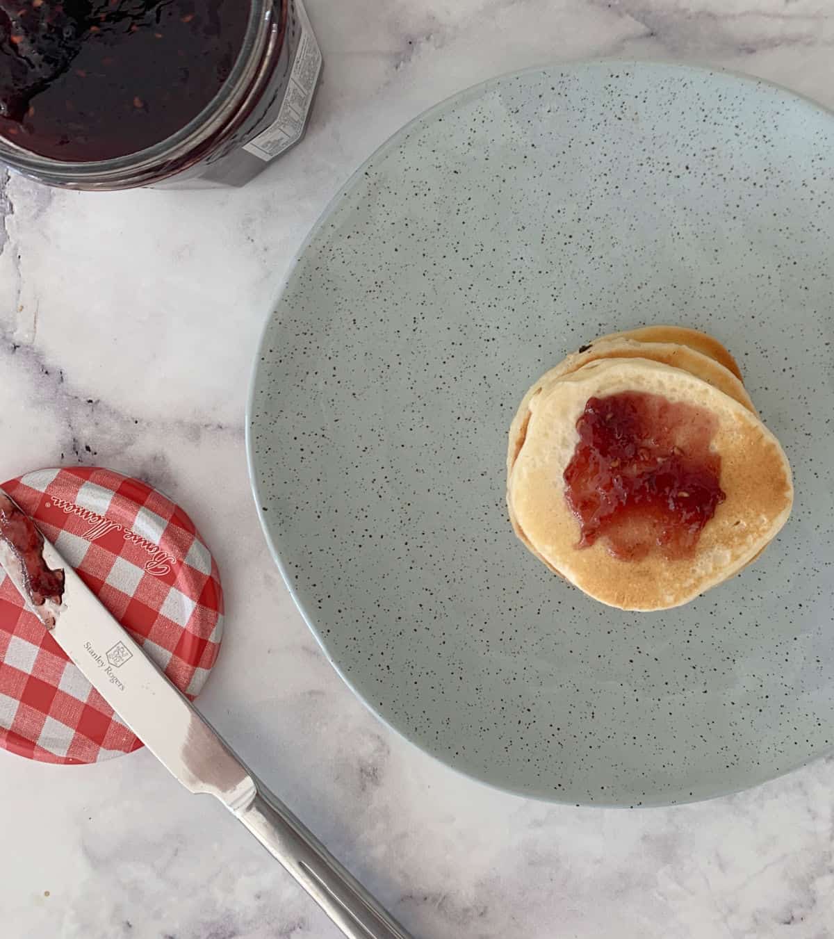 Pikelets topped with raspberry jam sitting on a greens speckled plate.