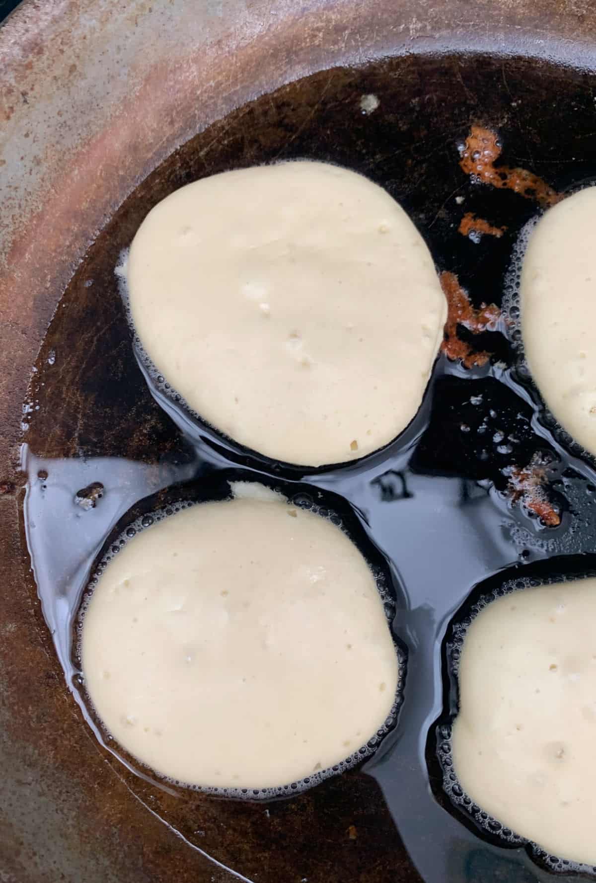 Pikelets cooking in a cast iron frying pan.