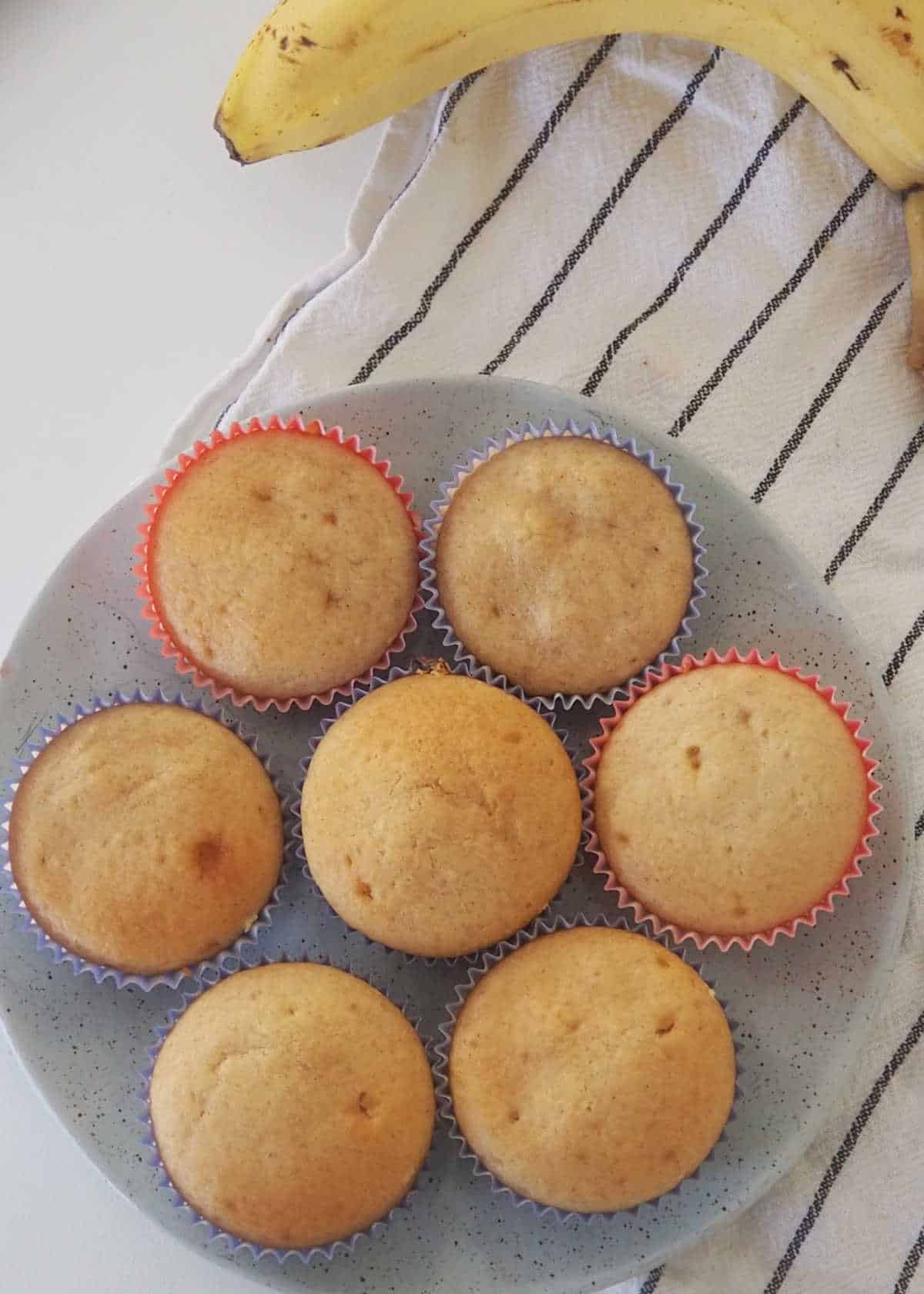 plate of banana muffins on a white and blue tea towel.