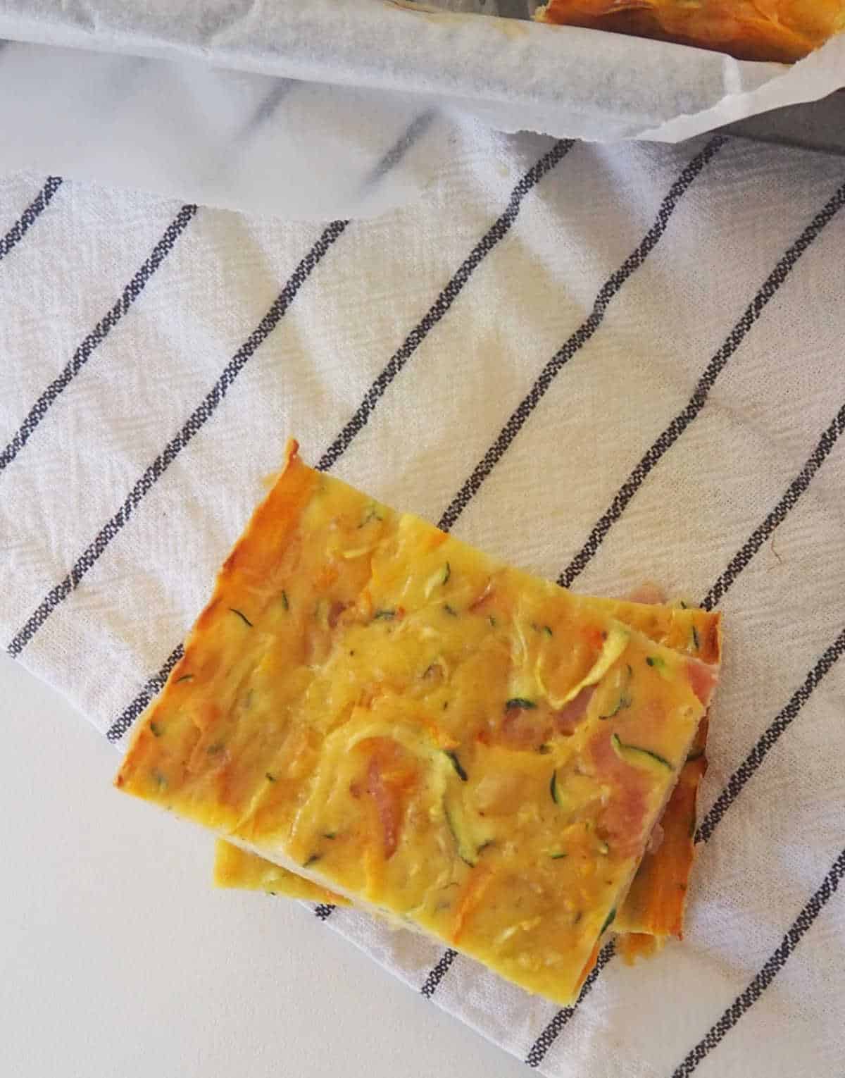 Two pieces of zucchini slice sitting on white and blue striped tea towel.
