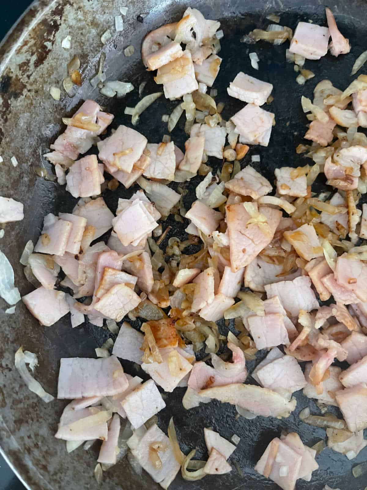 Bacon and onion cooking in a frying pan.