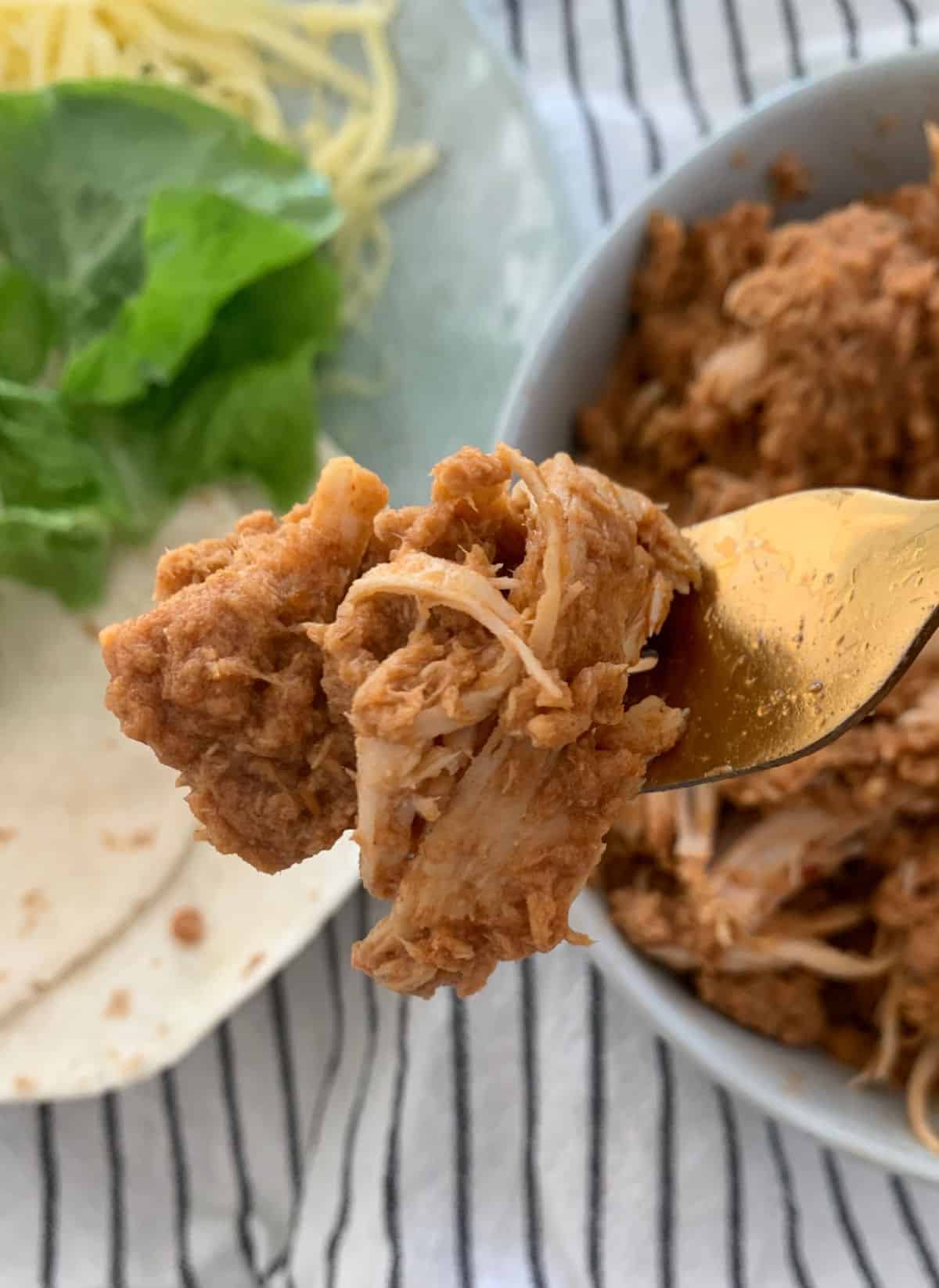 Gold fork holding up shredded Mexican chicken.