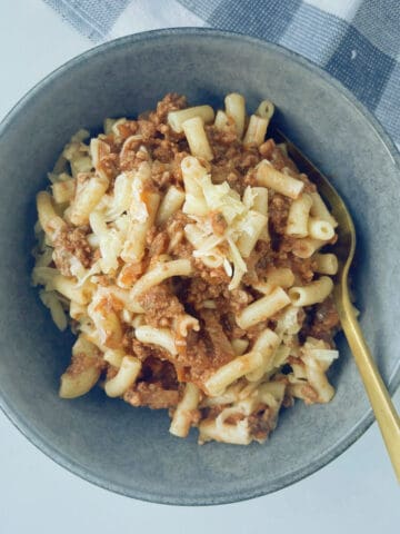 Pasta Bake made in a slow cooker sitting in a grey speckled bowl with a gold spoon in it.