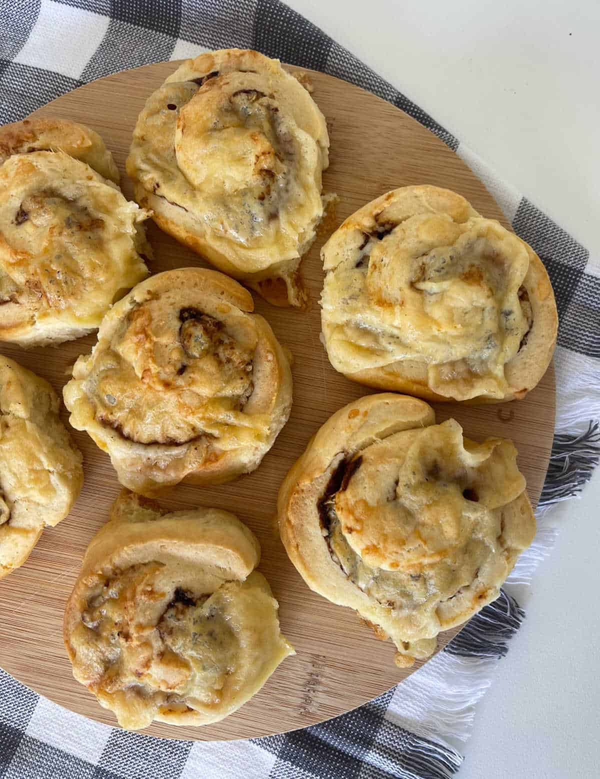 Overhead view of seven Vegemite and cheese scrolls on a round wooden board.