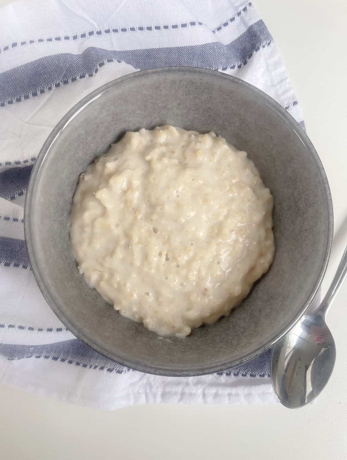 Porridge in a grey bowl with silver spoon next to it.