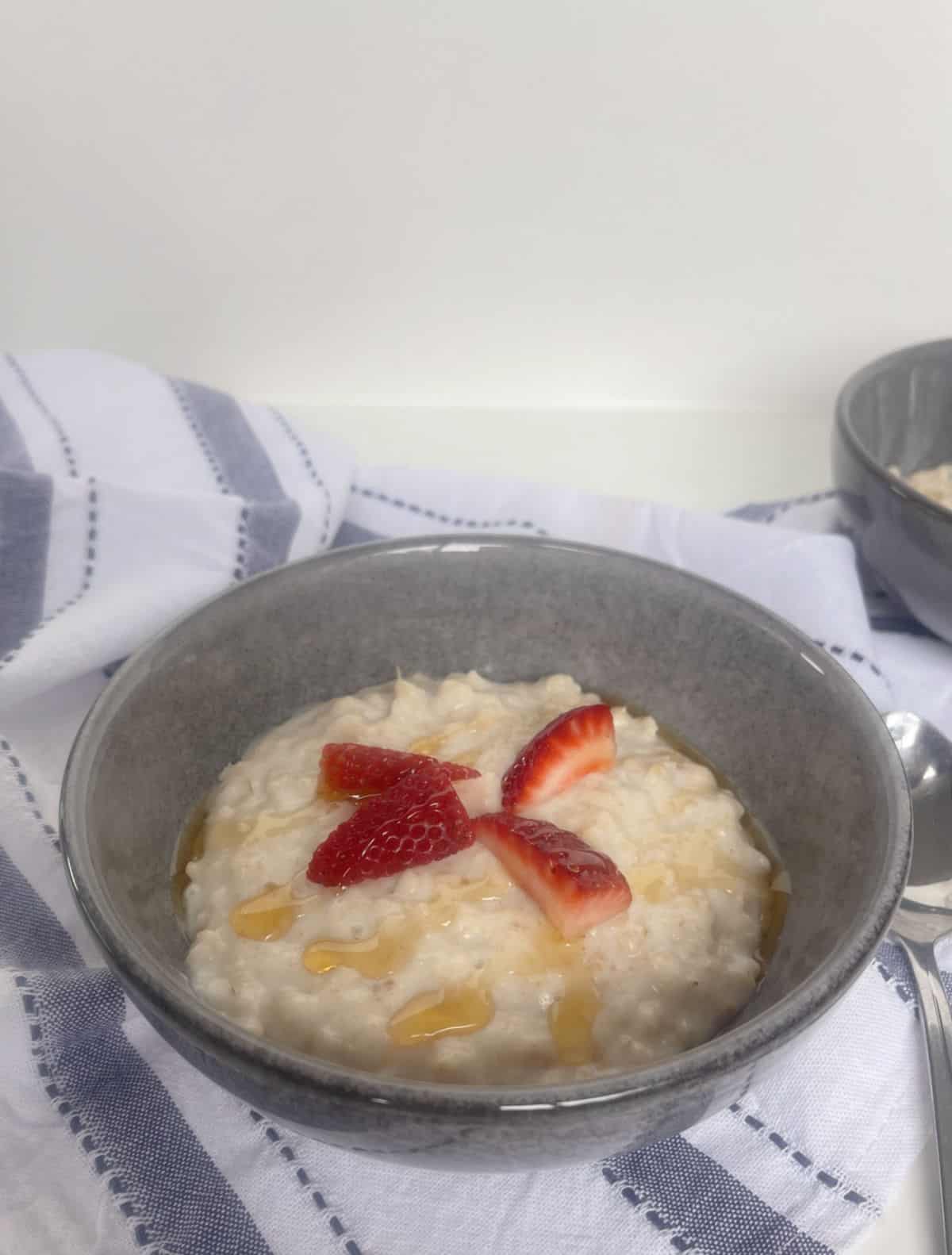 side view of Porridge topped with honey and strawberries in a grey bowl.